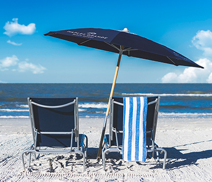 Frankford Avalon beach umbrella shading two beach chairs laying in the sand by the shore in Naples, Florida.
