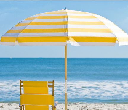 Frankford Avalon Beach umbrella with yellow striped fabric set up on the sand next to yellow beach lounger